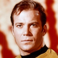 William Shatner in yellow shirt in front of red background